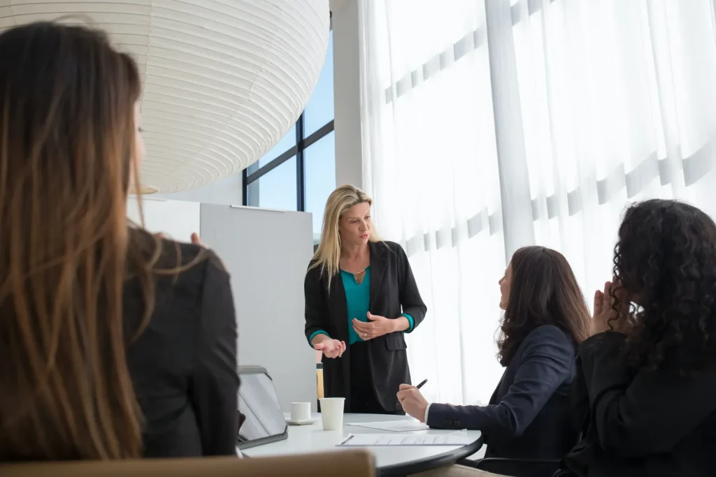 Lady in a green top, with a black jacket presenting at a meeting.