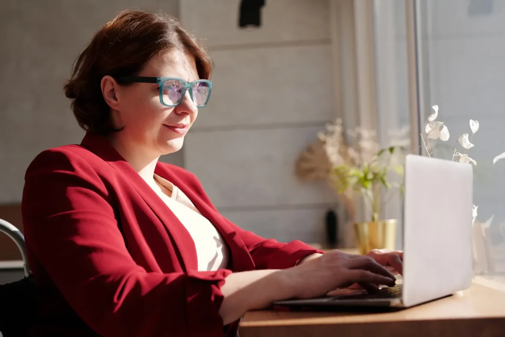 Lady in a red jacket, with glasses, sitting at a laptop