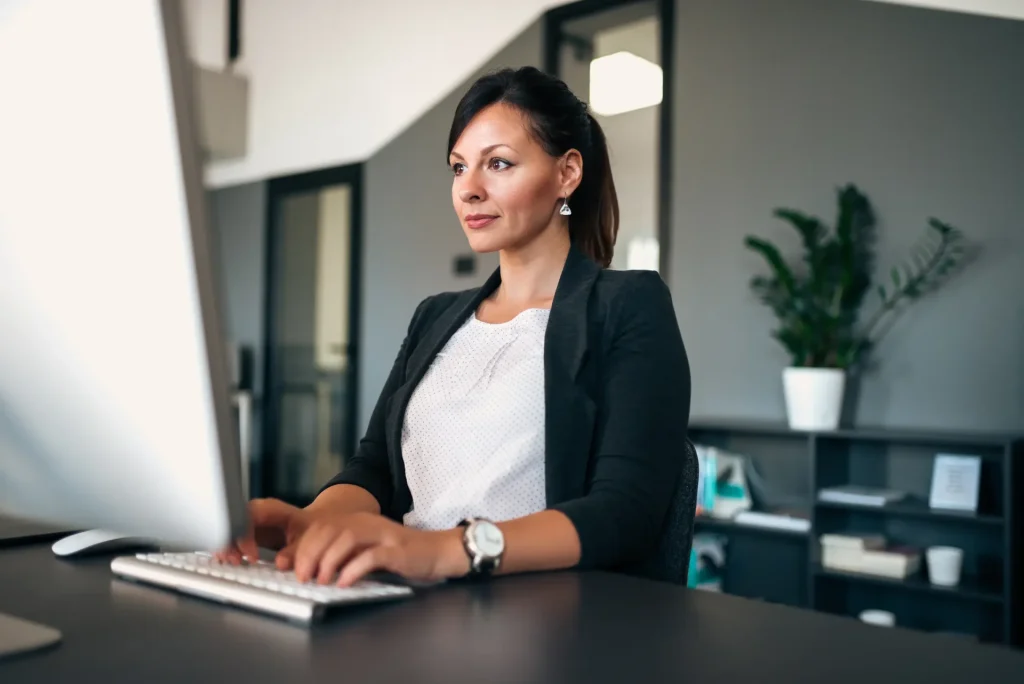 Lady in business jacket typing at desktop computer