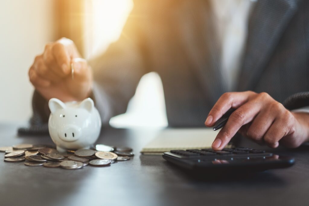 Closeup image of a woman putting coins in a piggy bank and calculating with calculator for saving money and financial concept